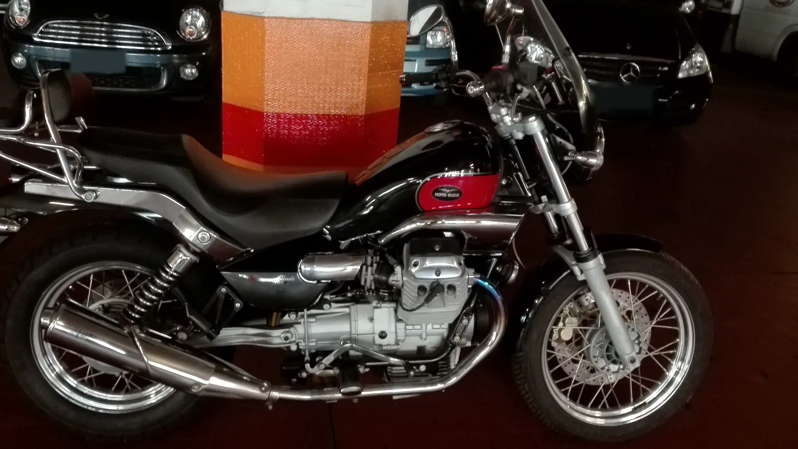 Una moto parcheggiata dentro l'autorimessa, accanto a un pilastro a fasce arancio e rosse